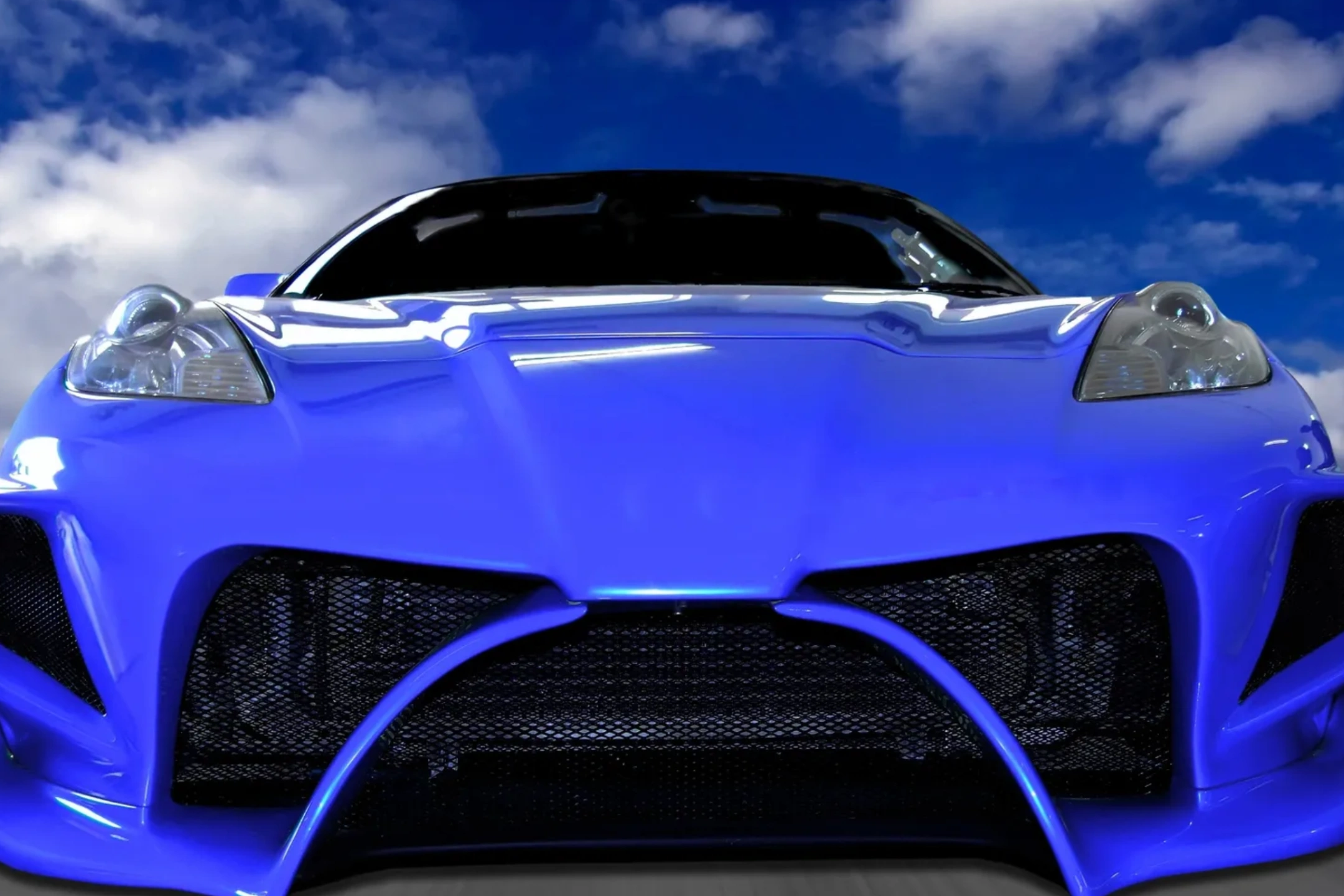 Close-up of a sleek blue sports car front under a partly cloudy sky.